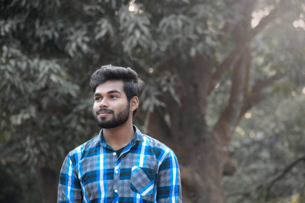 A young asian indian boy looking at the other side in front of natural background with blue check shirt